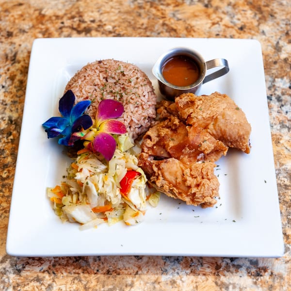 Dunns River Island Cafe's fried chicken with rice, steamed vegetables, and gravy, garnished with orchids.
