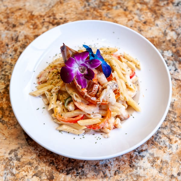 Dunns River Island Cafe's lobster penne pasta with red peppers, garnished with purple and blue orchids.
