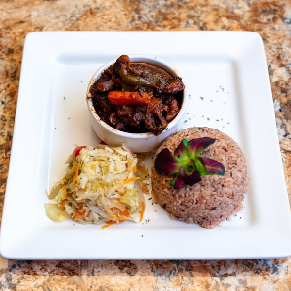 Dunns River Island Cafe's Jamaican stew, rice and peas, and steamed cabbage on a white plate.