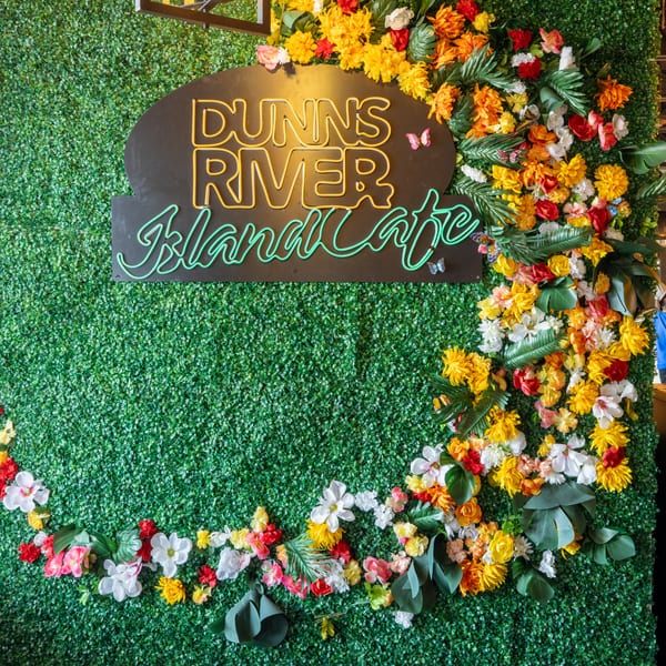 Dunns River Island Cafe neon sign on a green wall with colorful flowers and butterflies.