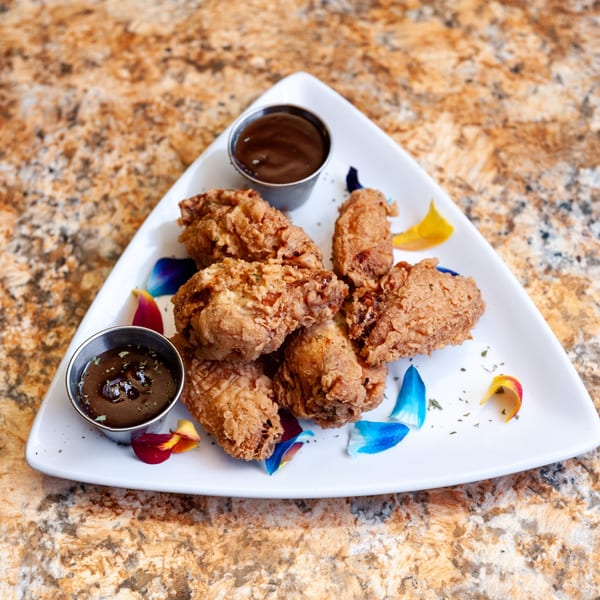 Crispy fried chicken wings with two dipping sauces and colorful flower petals on a white plate.