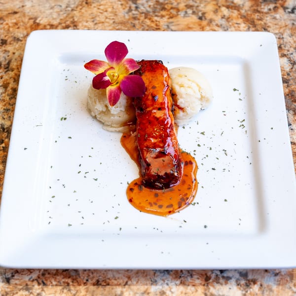 Glazed salmon with mashed potatoes and an orchid garnish on a white plate.