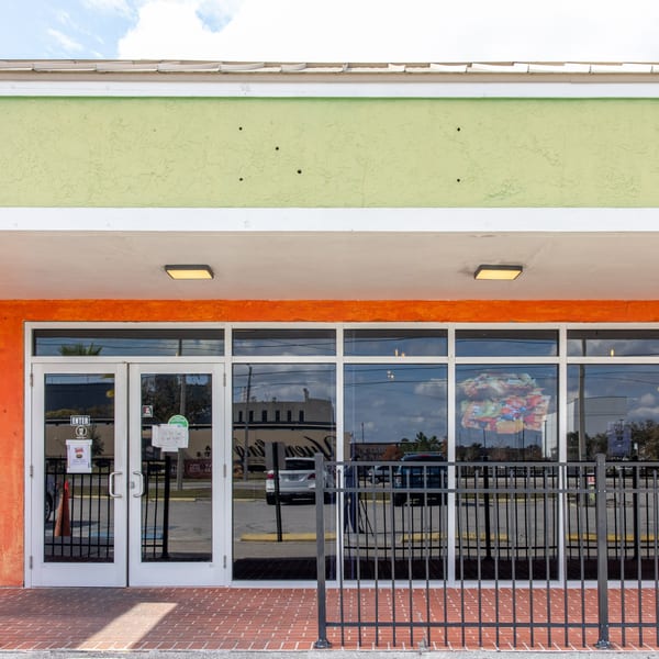 Exterior of Dunns River Island Cafe, with a bright orange and green facade, glass doors, and a black fence.