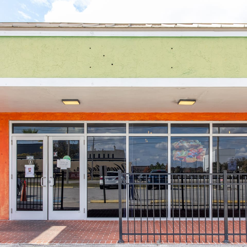 Exterior of Dunns River Island Cafe, with a bright orange and green facade, glass doors, and a black fence.
