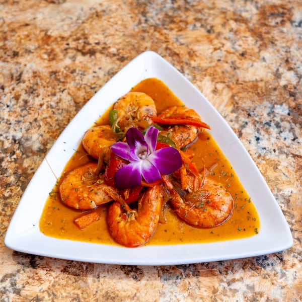 Dunns River Island Cafe's Jamaican curry shrimp dish, garnished with a purple orchid, on a white triangular plate.